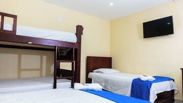 Une chambre d’hôtel avec deux lits simples, un lit superposé en bois, un téléviseur à écran plat fixé au mur et un couvre-lit bleu.