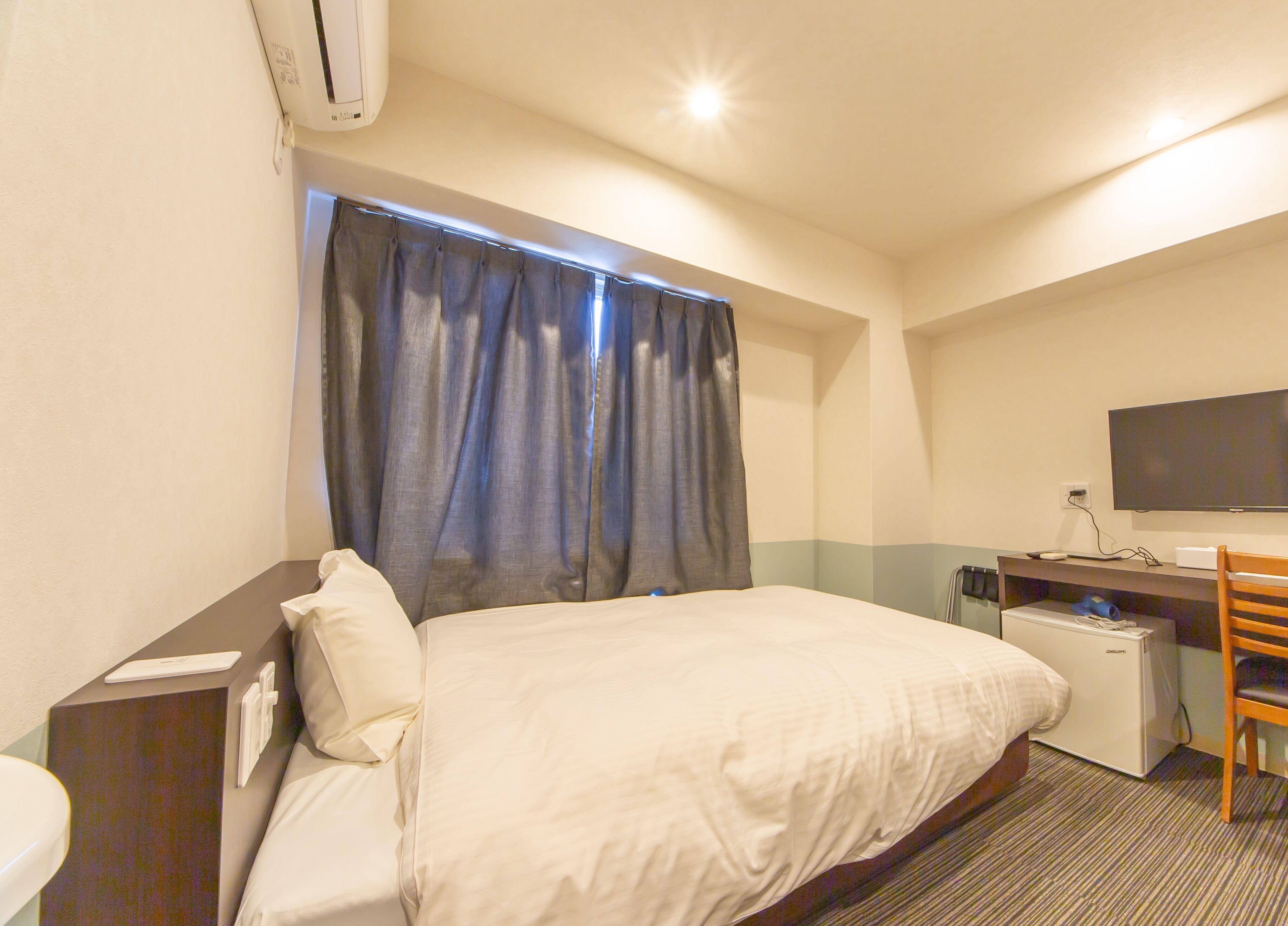 A hotel room with a bed, a desk with a computer, a television, and a window with curtains.