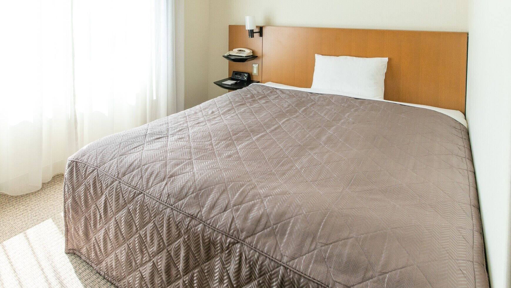 Habitació d'hotel amb llit, una nit, un telèfon i una làmpada penjada a la paret.