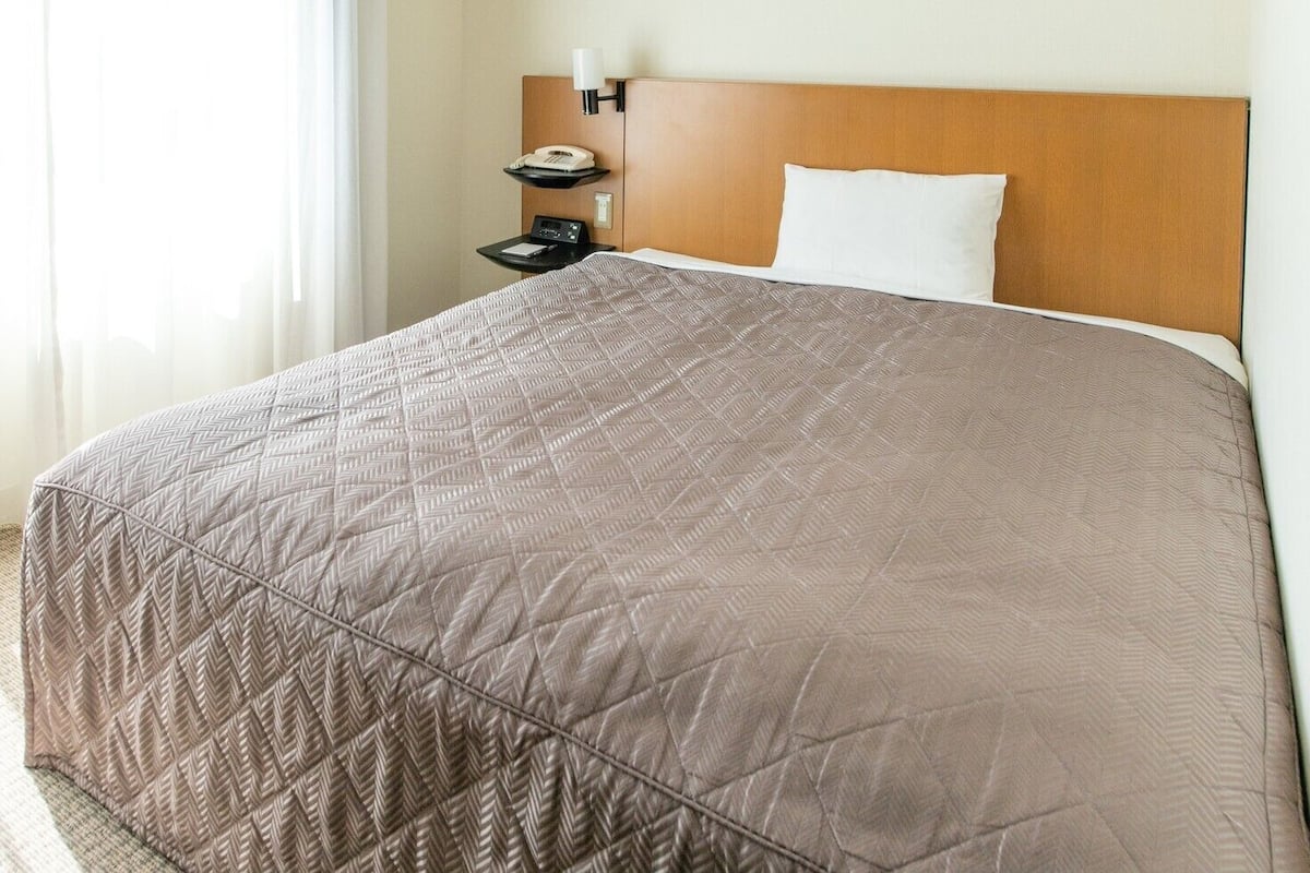 Ein Hotelzimmer mit Bett, Nachttisch, Telefon und Wandlampe.