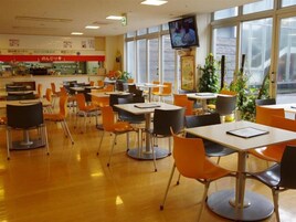 Una cafetería con mesas y sillas, una pantalla de televisión y un mostrador con alimentos.
