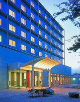Un hotel de varios pisos con fachada azul, un acceso cubierto y un patio de grava.