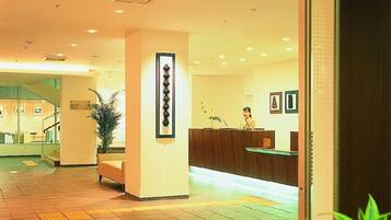 A hotel reception area with a reception desk, a staircase, and a potted plant.