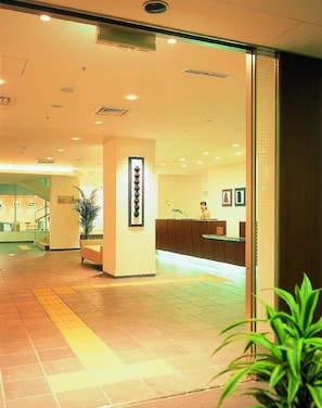 Zona de recepción de un hotel, con mostrador, escalera y una planta en maceta.