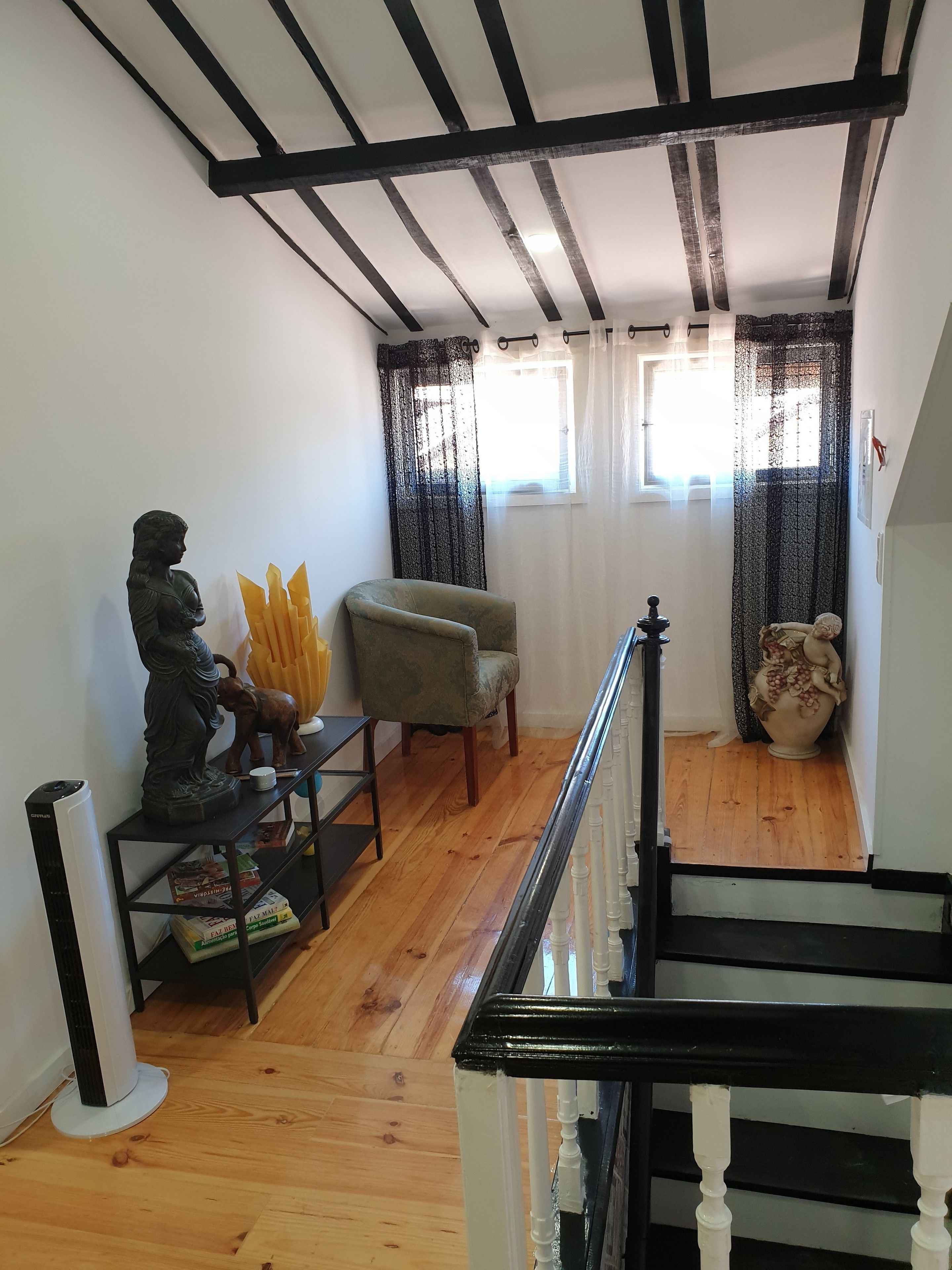 A room with a wooden floor, a statue, a chair, and a staircase with white balusters.