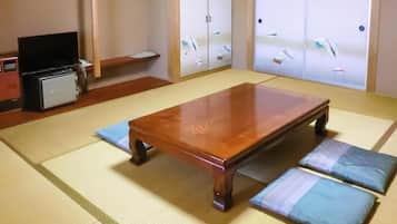 A tatami mat room with a wooden table, cushions, a television, and a small cabinet.