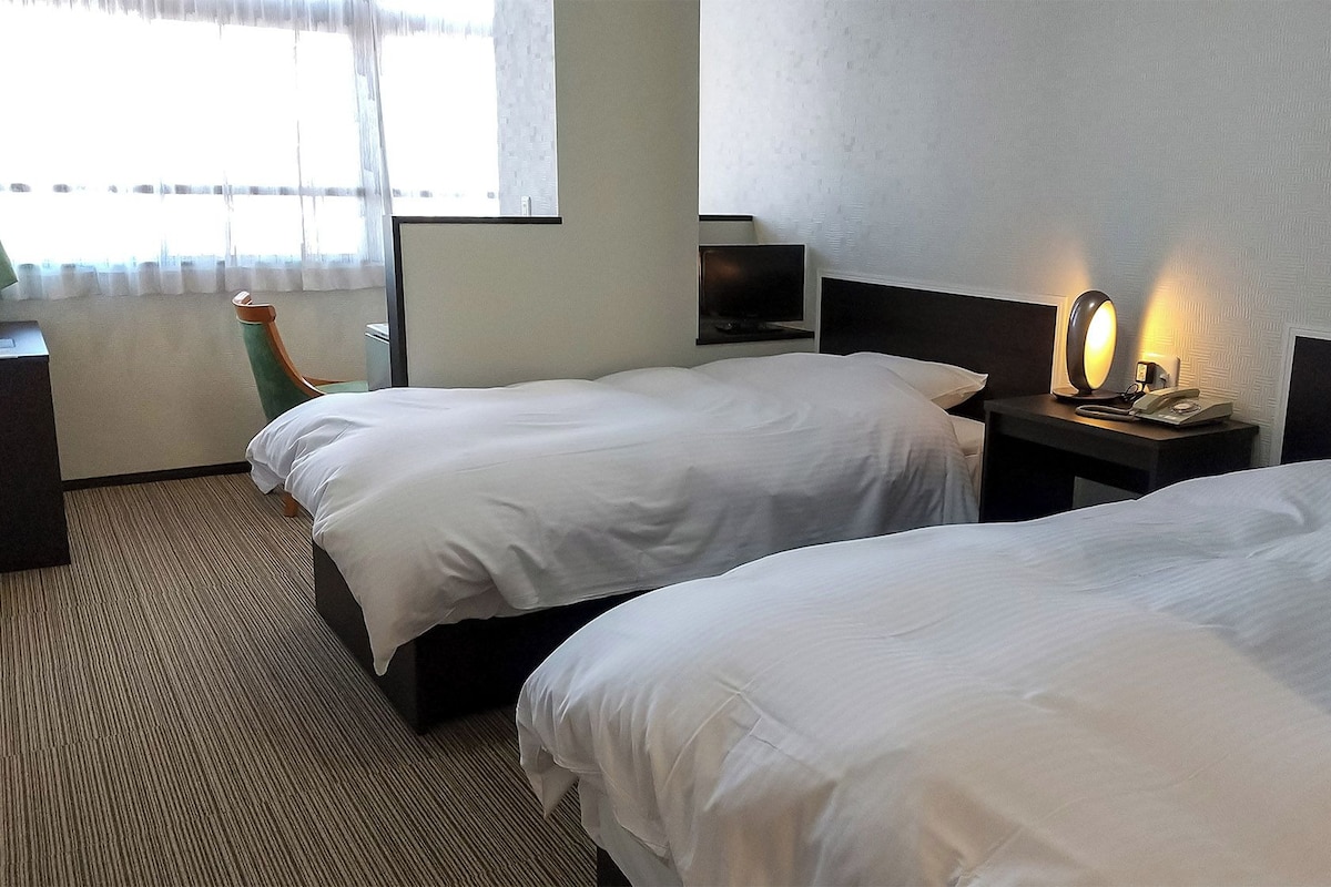 Une chambre d’hôtel avec deux lits, un bureau, une chaise, une télévision et une lampe de chevet.