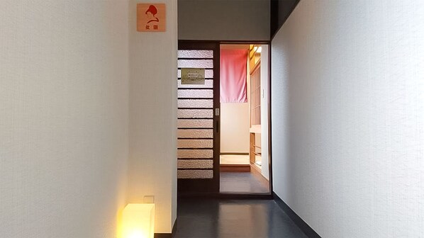 Un couloir étroit avec une porte en bois qui mène à une pièce. Une enseigne avec des caractères japonais est visible sur le mur.