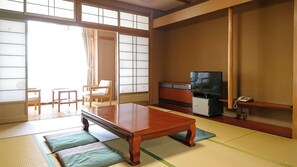 A traditional Japanese room with tatami flooring, a low wooden table, a television, and a small cabinet.