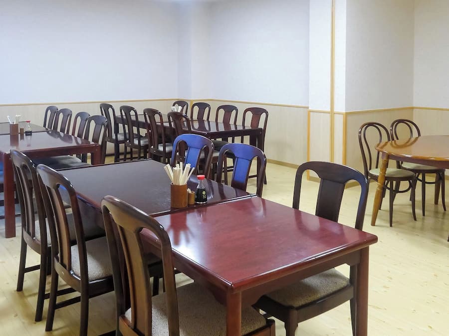 A conference room with multiple tables and chairs, a wooden floor, and a plain wall.