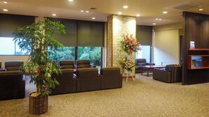 A reception area with a large potted plant, seating, a decorative flower arrangement, and a wall-mounted TV. - Daionji Onsen Banshokaku (Fukui)
