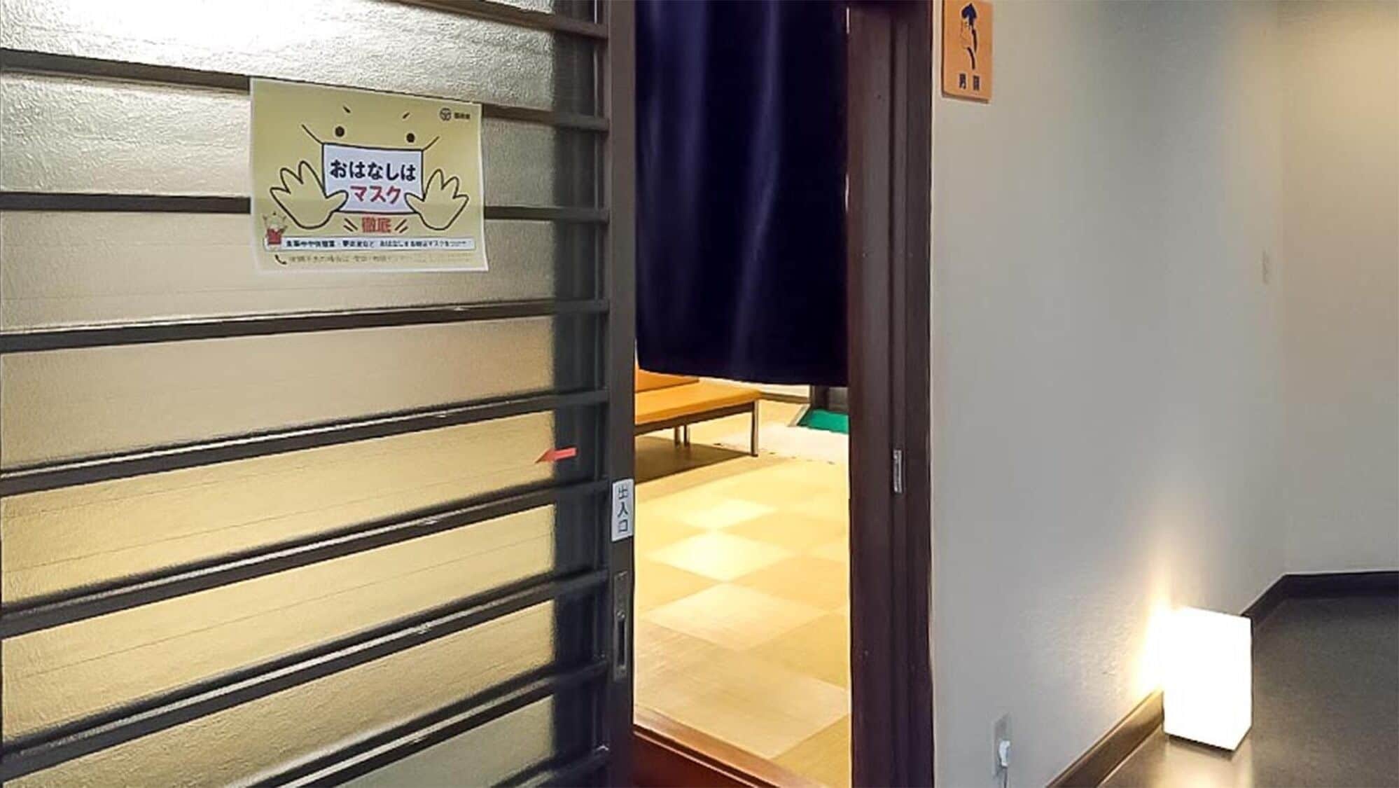 Quarto com porta deslizante, um banco e interruptor de luz na parede. Há também uma placa com texto em japonês.