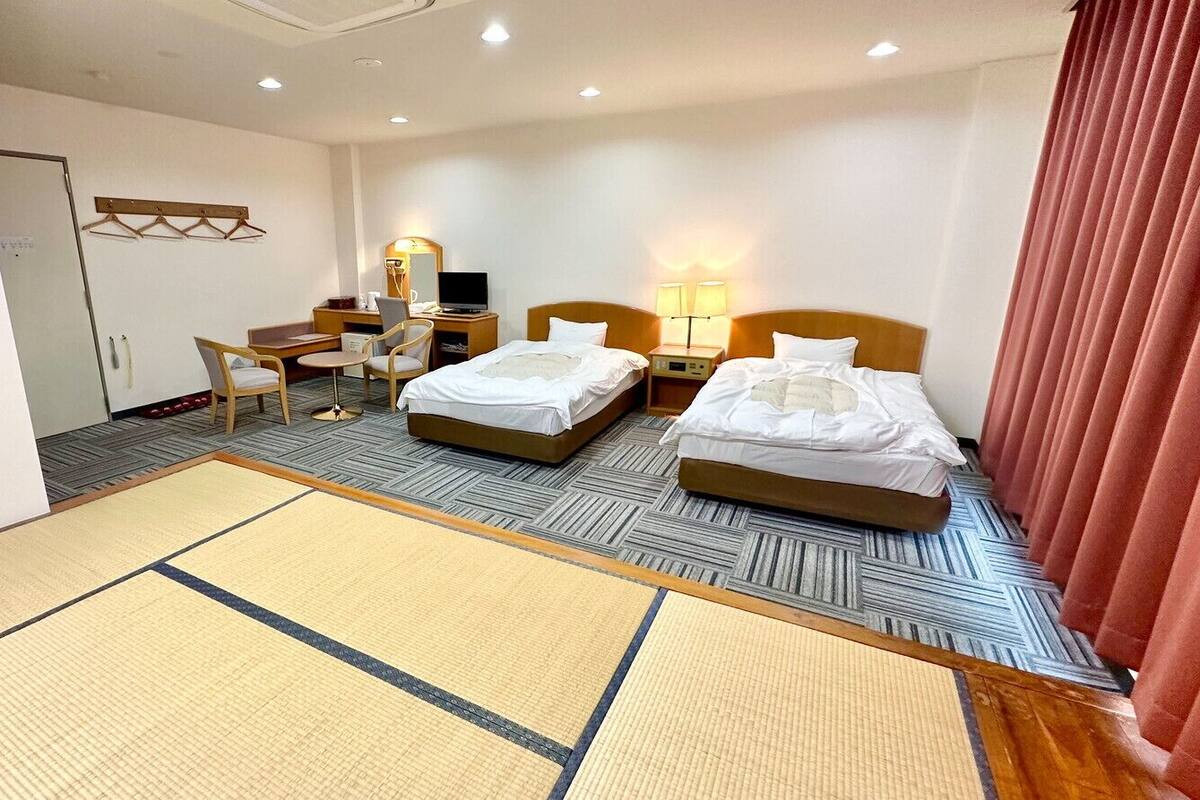 A hotel room with two beds, a desk, a chair, a TV, and a mirror.