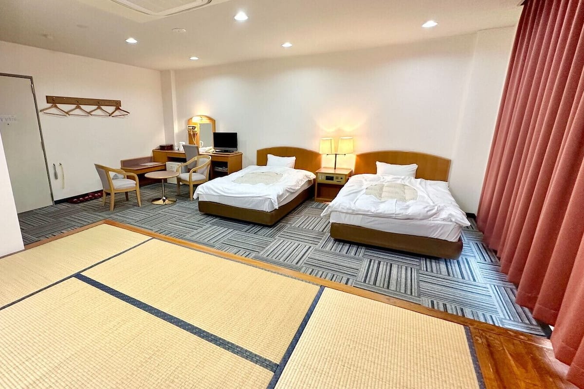 A hotel room with two beds, a desk, a chair, a TV, and a mirror.