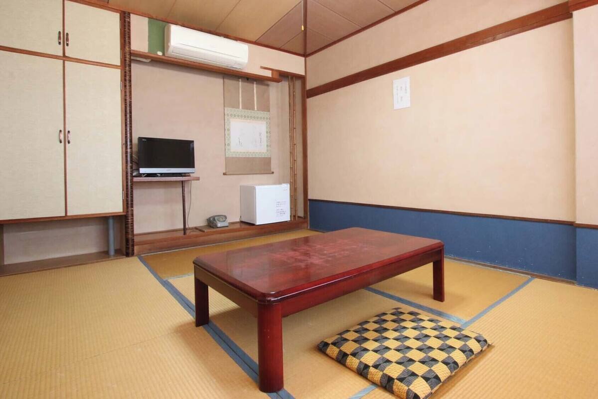 A tatami mat room with a wooden table and a cushion, a television, and a small cabinet.