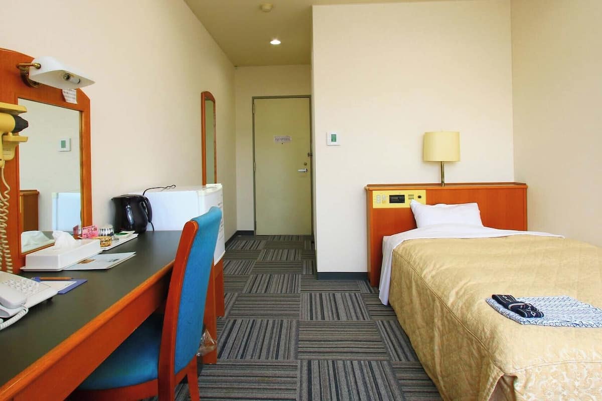A hotel room with a desk, chair, bed, and a mirror.