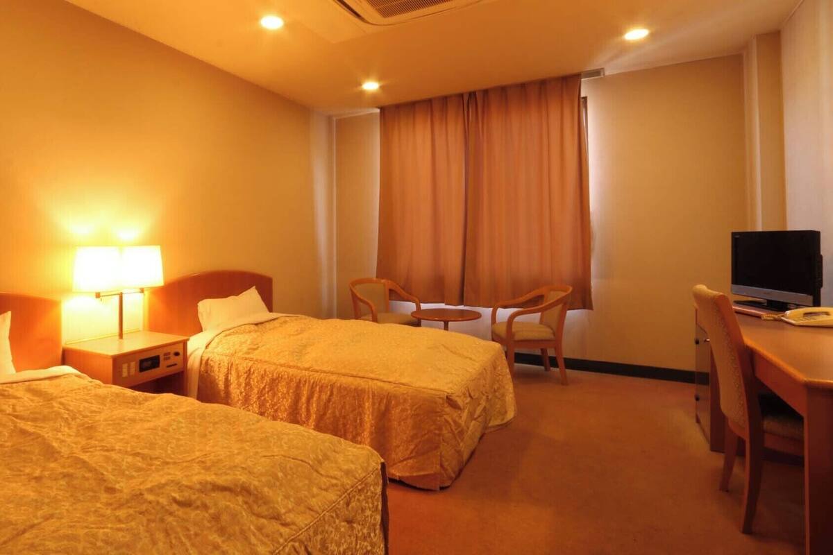 A hotel room with two beds, a desk with a computer, a chair, and a TV.