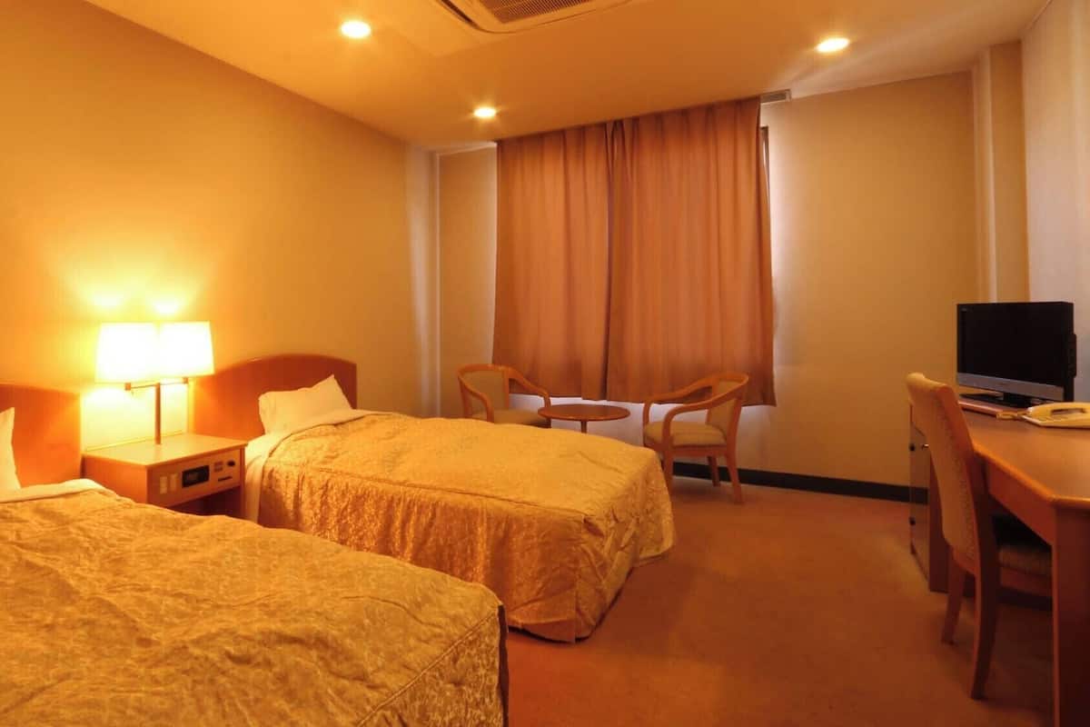 A hotel room with two beds, a desk with a computer, a chair, and a TV.