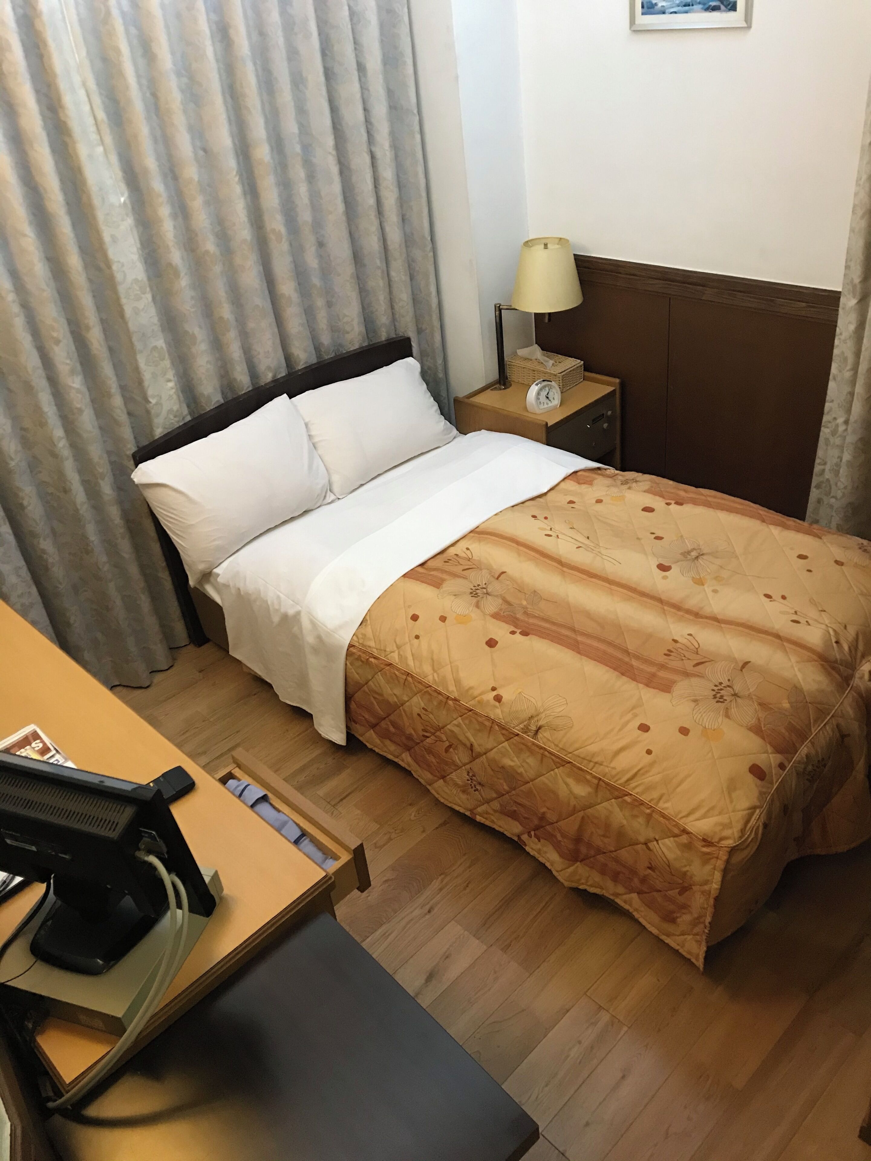 A hotel room with a bed, a bedside table with a lamp, a clock, and a small basket.
