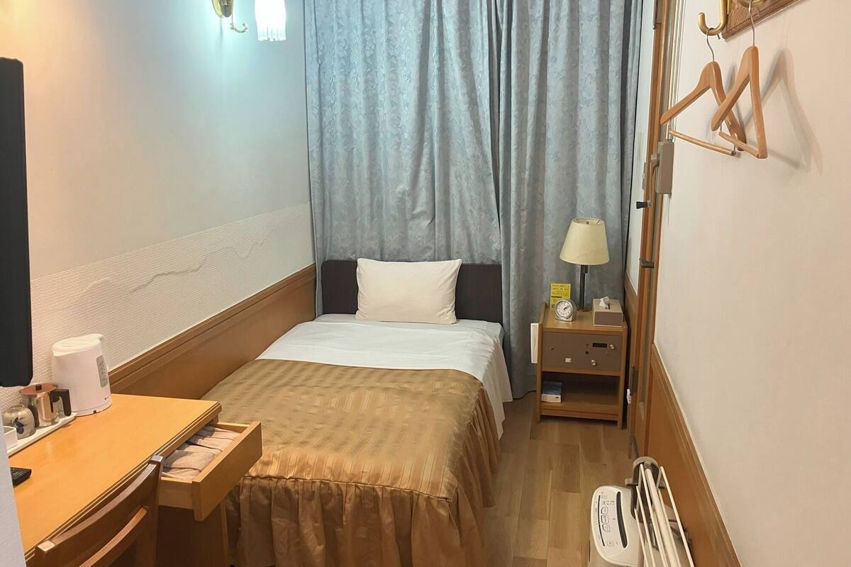 Ein Hotelzimmer mit Bett, Nachttisch, Lampe und Schreibtisch mit Stuhl.