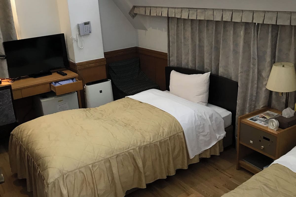 Ein Hotelzimmer mit einem Bett, einem Schreibtisch mit Fernseher, einem Telefon und einem Nachttisch mit Lampe.