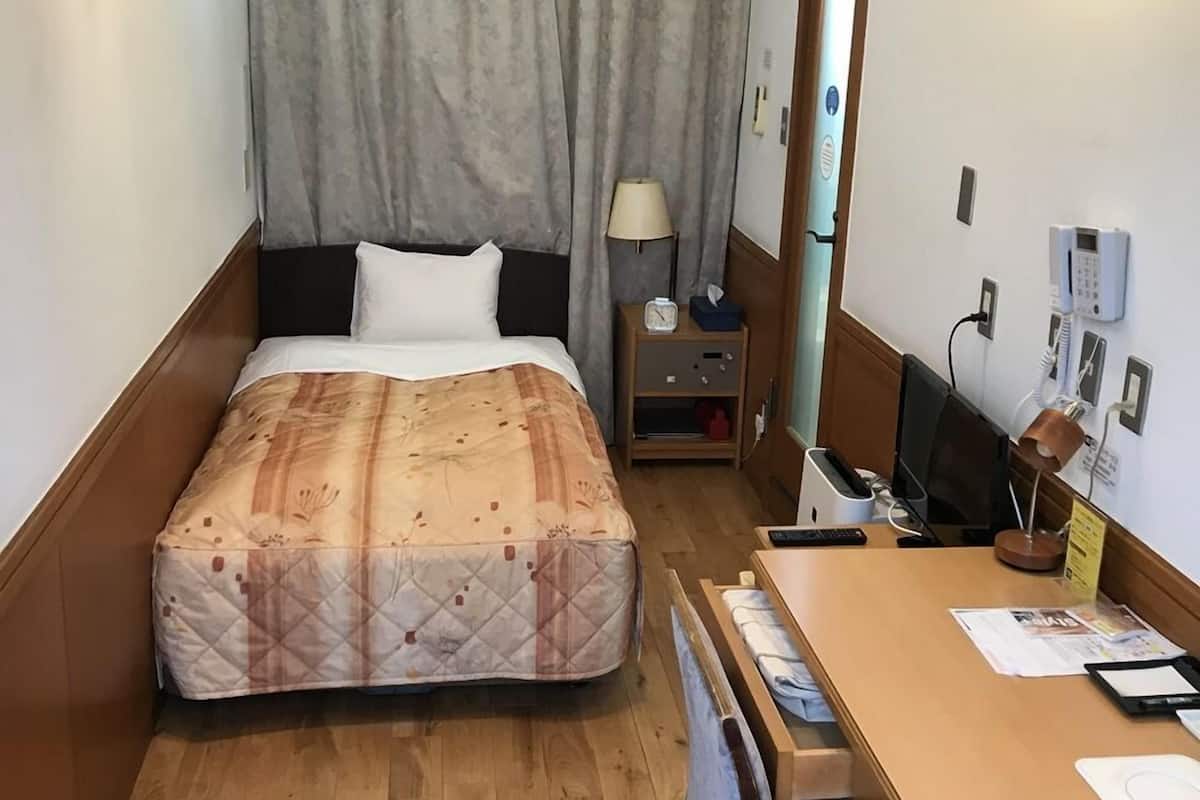 Ein Hotelzimmer mit Bett, Schreibtisch, Stuhl, Lampe, Telefon und Spiegel.