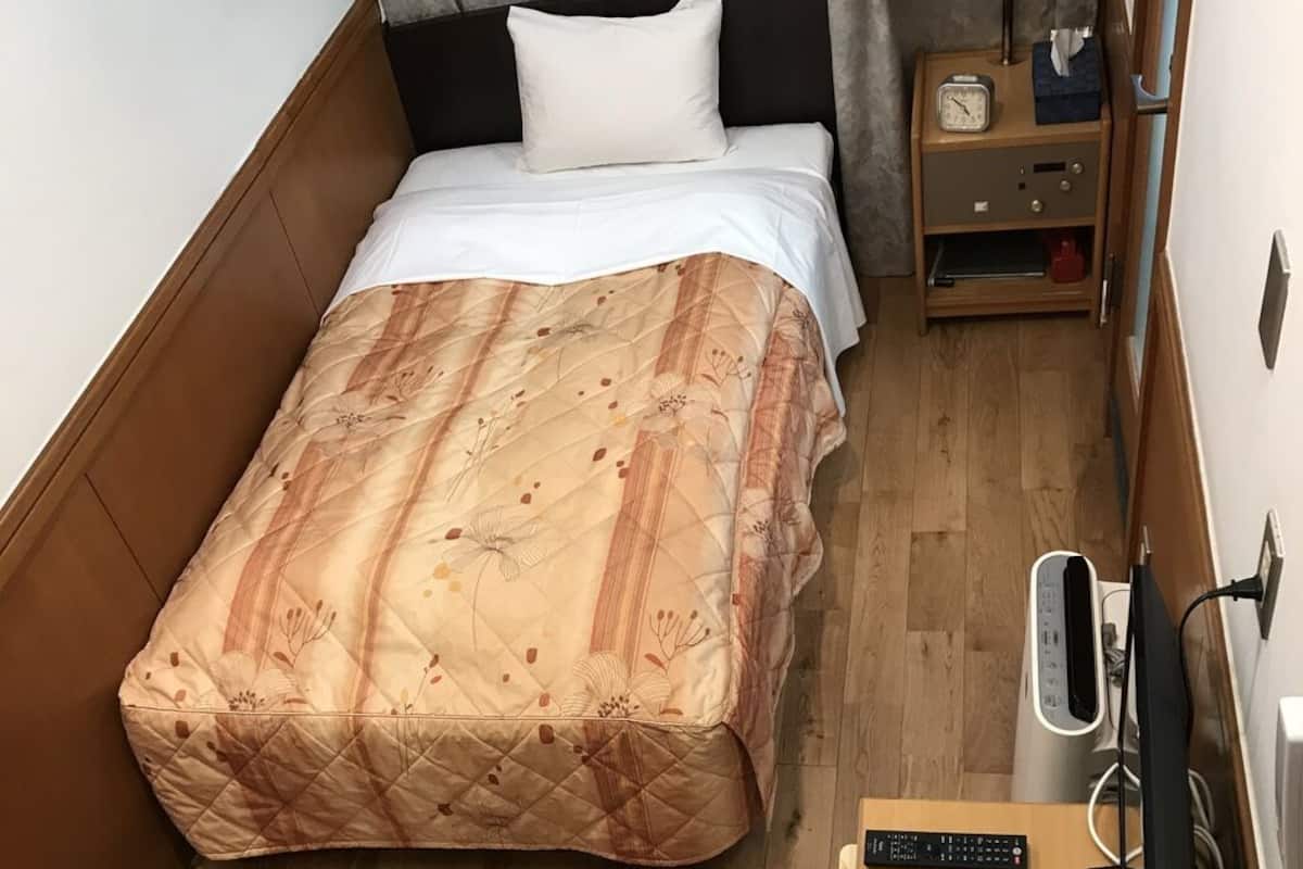 Ein Hotelzimmer mit einem Bett, einem Nachttisch mit Lampe, einer Uhr und einem TV-Schrank mit Fernbedienung.