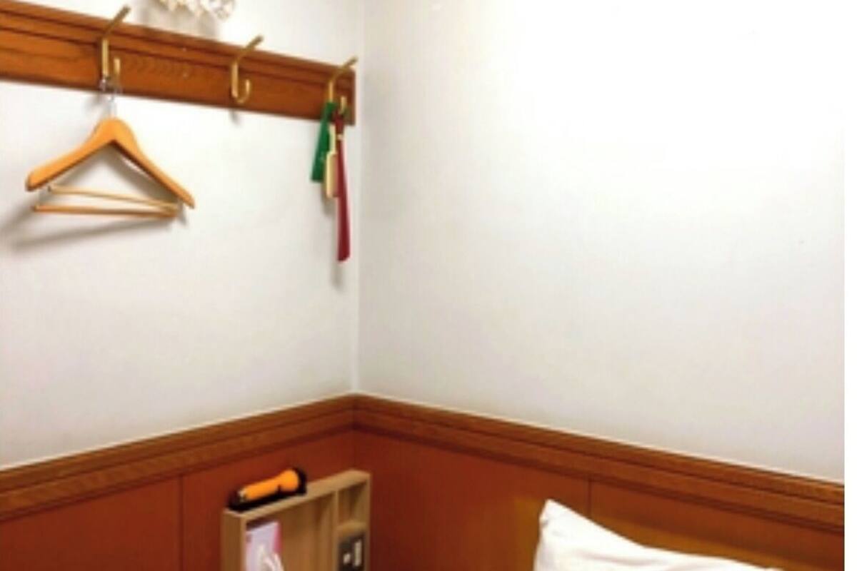 Ein Hotelzimmer mit einem Bett, einem Holzkopfteil, einem Ablagefach mit Toilettenartikeln und einem an der Wand befestigten Kleiderhaken.
