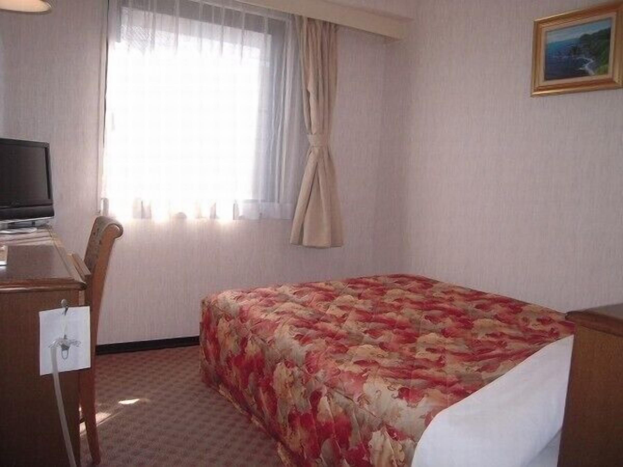 A hotel room with a bed, a desk, a television, and a window with curtains.