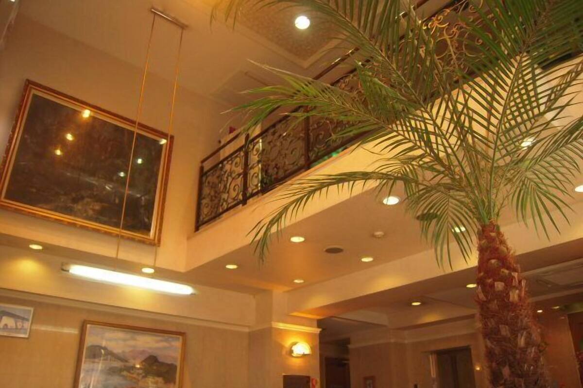 A lobby with a palm tree, a framed painting, and a reception desk.