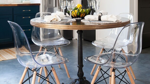 Une cuisine moderne avec une table de salle à manger ronde, des chaises transparentes et un panier de fruits.
