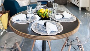 Un coin repas avec une table ronde dressée pour quatre personnes, un lustre, un canapé et un téléviseur posé sur un meuble blanc.