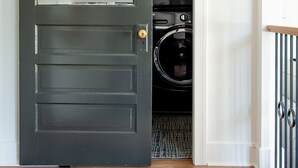 Une porte en bois sombre, de style « porte de grange » coulissante, qui donne sur une buanderie où sont empilées les machines à laver.