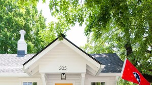 Une maison blanche avec une porte jaune, le numéro 305, et un drapeau rouge sur la droite.