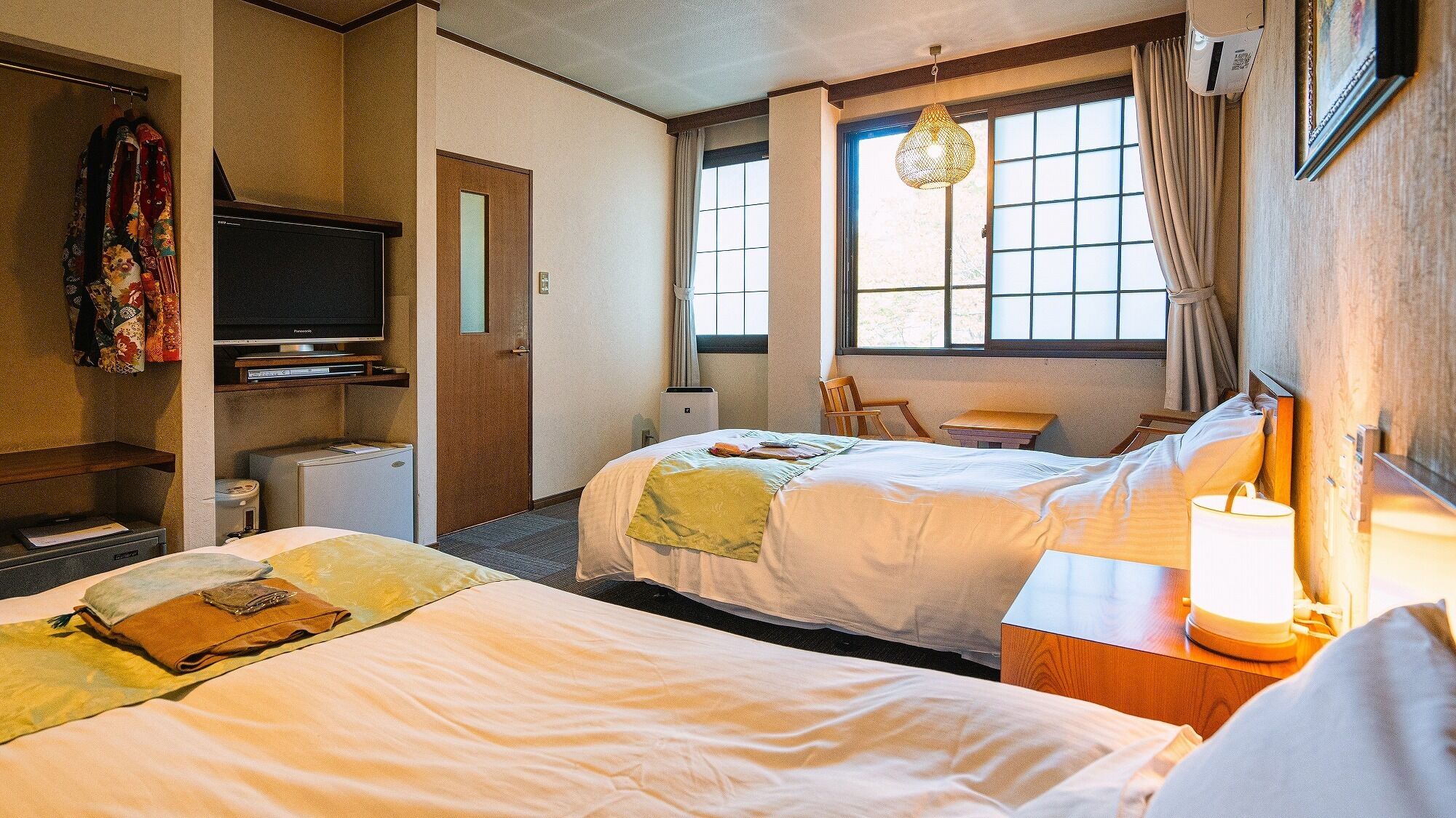 Ein Hotelzimmer mit zwei Betten, einem Fernseher, einem Schreibtisch, einem Stuhl und einem Fenster mit Vorhängen.