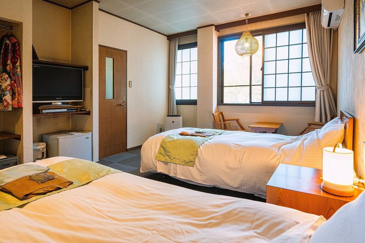 A hotel room with two beds, a television, a desk, a chair, and a window with curtains.