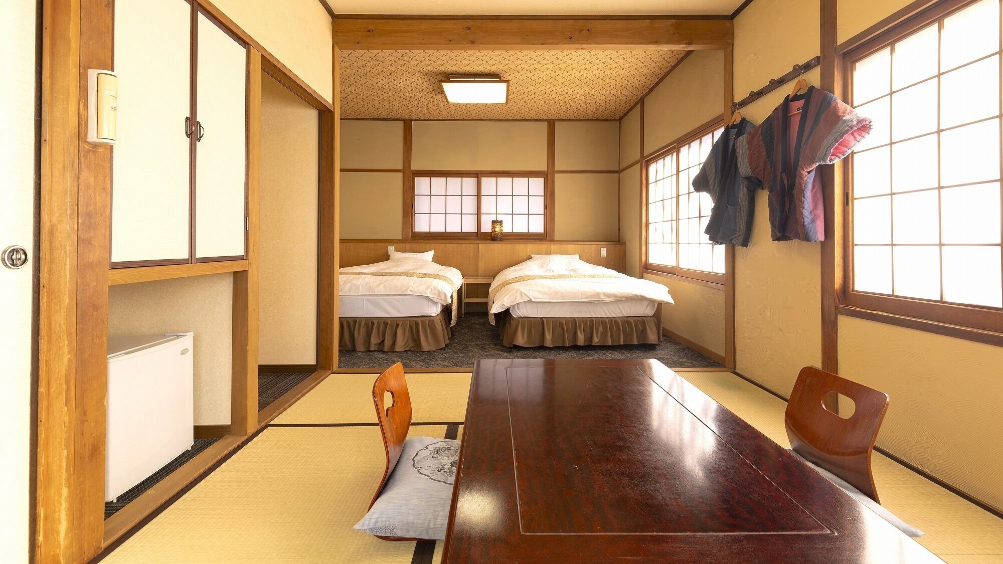 Ein traditioneller japanischer Raum mit Tatami-Boden, zwei Betten, einem Holztisch und einer Schiebetür.