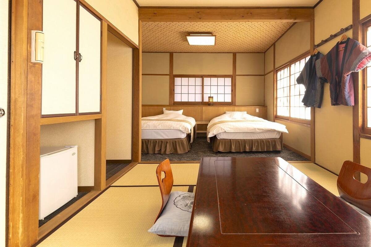 A traditional Japanese room with tatami flooring, two beds, a wooden table, and a sliding door.