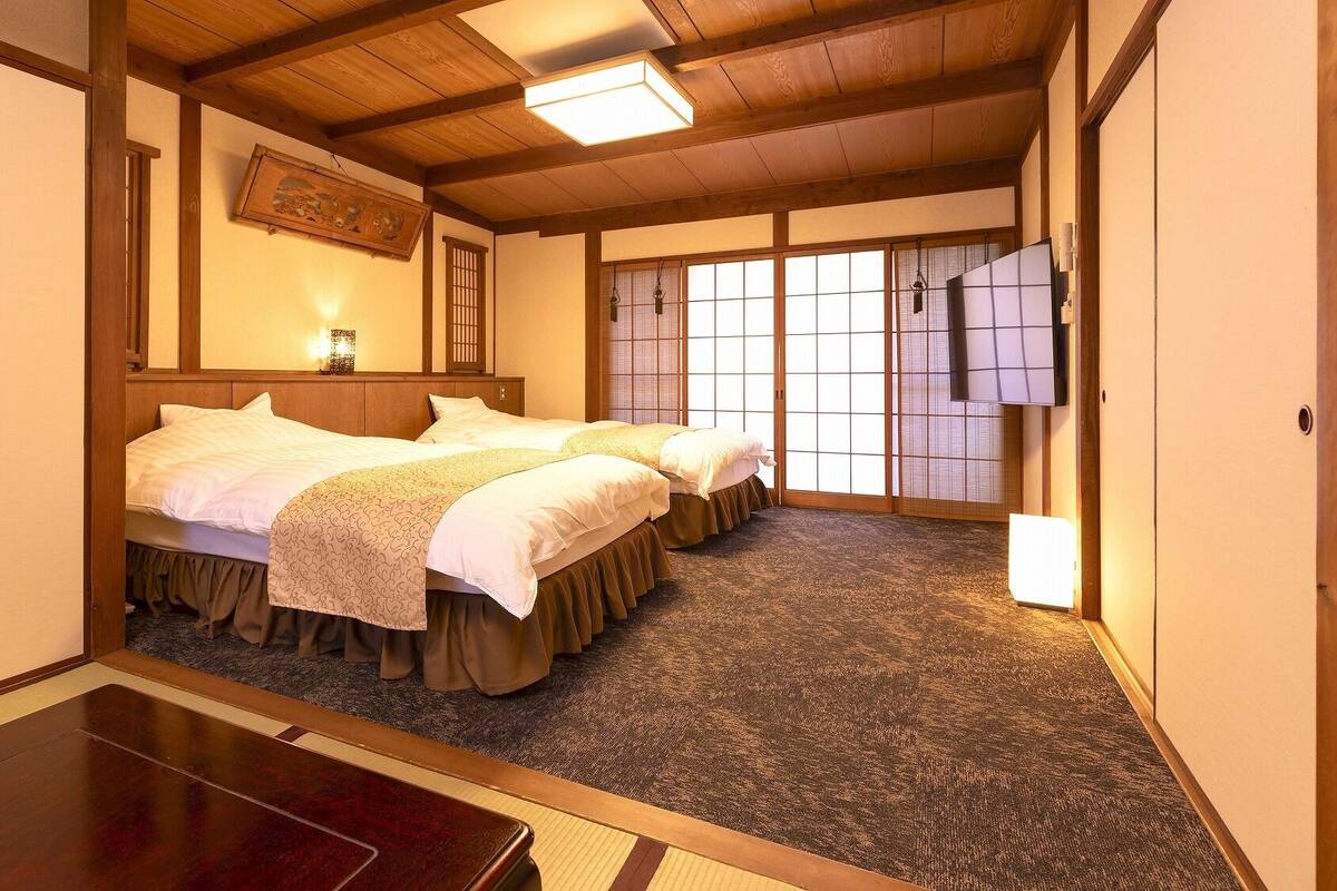 A traditional Japanese-style hotel room with a wooden ceiling, tatami flooring, and shoji screens.
