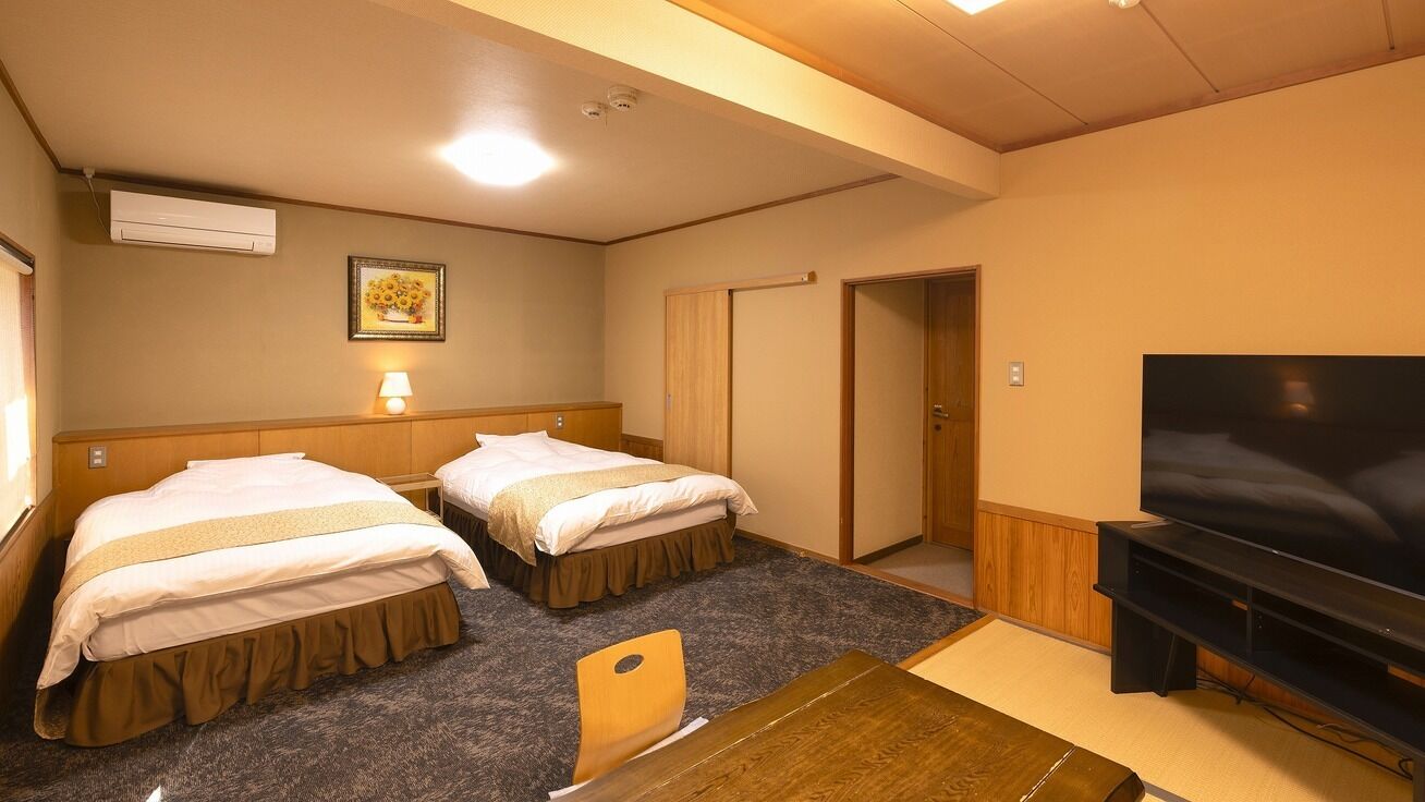 A hotel room with two beds, a television, a desk, and a door.
