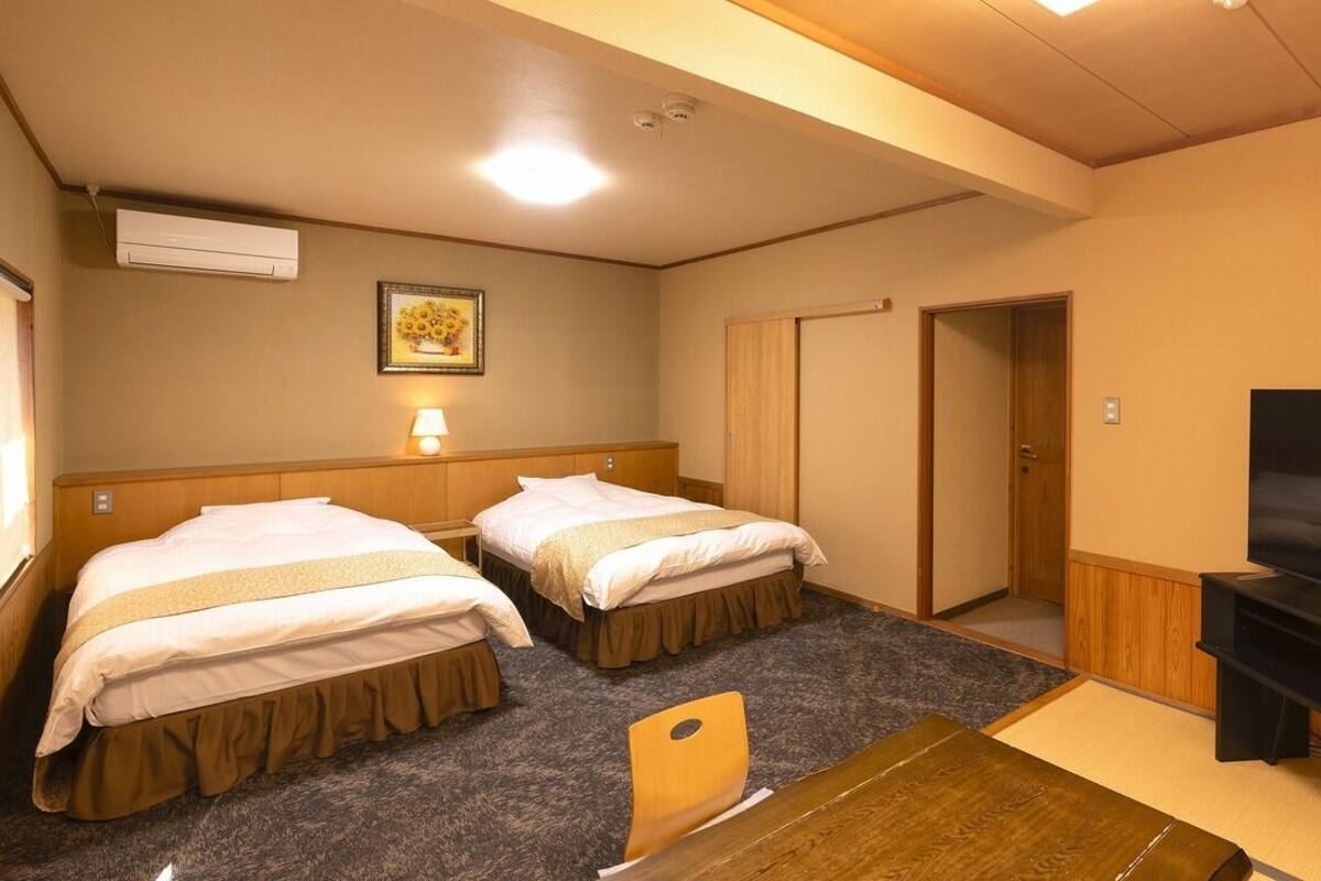 A hotel room with two beds, a television, a desk, and a door.
