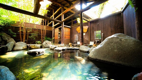 Un onsen japonés tradicional con interiores de madera, un manantial termal de piedra y vistas al bosque circundante.