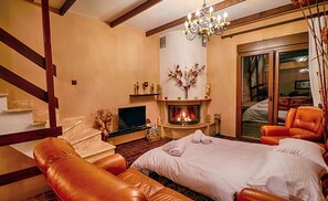 Relax in this inviting room with a large bed, fireplace, and comfortable sofa, offering a view of the outdoor area.