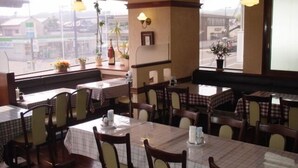 A restaurant with multiple tables and chairs, some with checkered tablecloths. There are potted plants on the windowsill and a view of the street outside. - Imabari Plaza Hotel (Imabari)