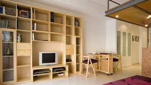Ein geräumiger Raum mit einem großen Bücherregal aus Holz, einem Fernseher, einem kleinen Tisch mit Stühlen und einem violetten Teppich.