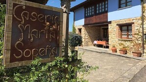 Een rustiek stenen bord met gebeeldhouwde tekst, een stenen gebouw met pannendak en bloempotten op de voorgrond.