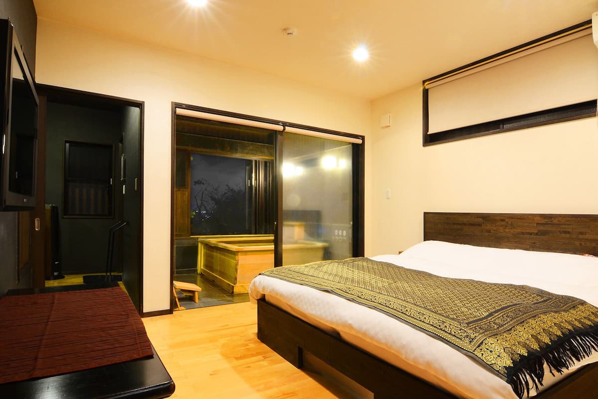 A bedroom with a bed, a TV, an air conditioner, and a sliding door leading to a bathroom.