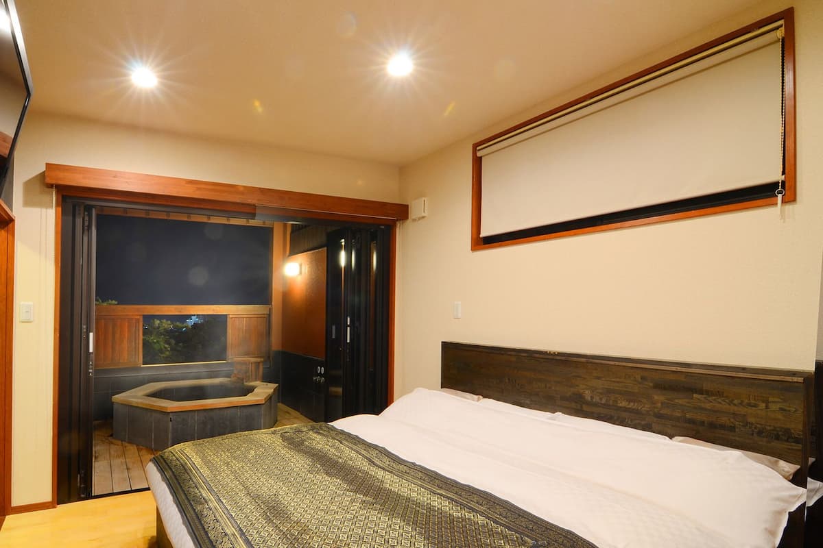 A bedroom with a bed, a TV, a bathtub, and a view of the outside.