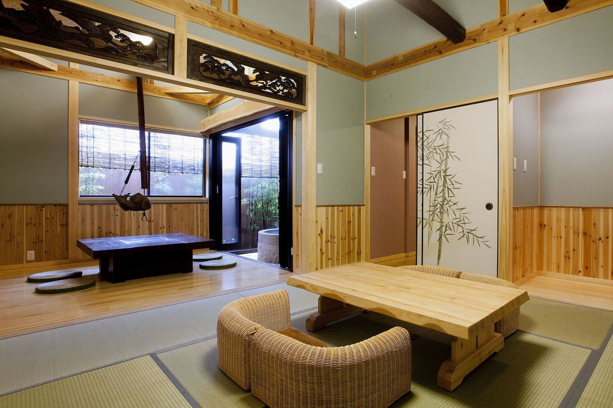 A traditional Japanese room with tatami flooring, a low table, a cushioned bench, sliding doors with bamboo paintings, and a hanging lantern.
