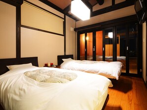 A hotel room with two beds, a large window, and a sliding door leading to a balcony. - Tokunoyado Fubuan (Beppu)